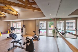 A gym with exercise bikes and cardio machines, wooden beams on the ceiling, and large windows with a view of the outside. - Les Bords de l'Aveyron (Negrepelisse)