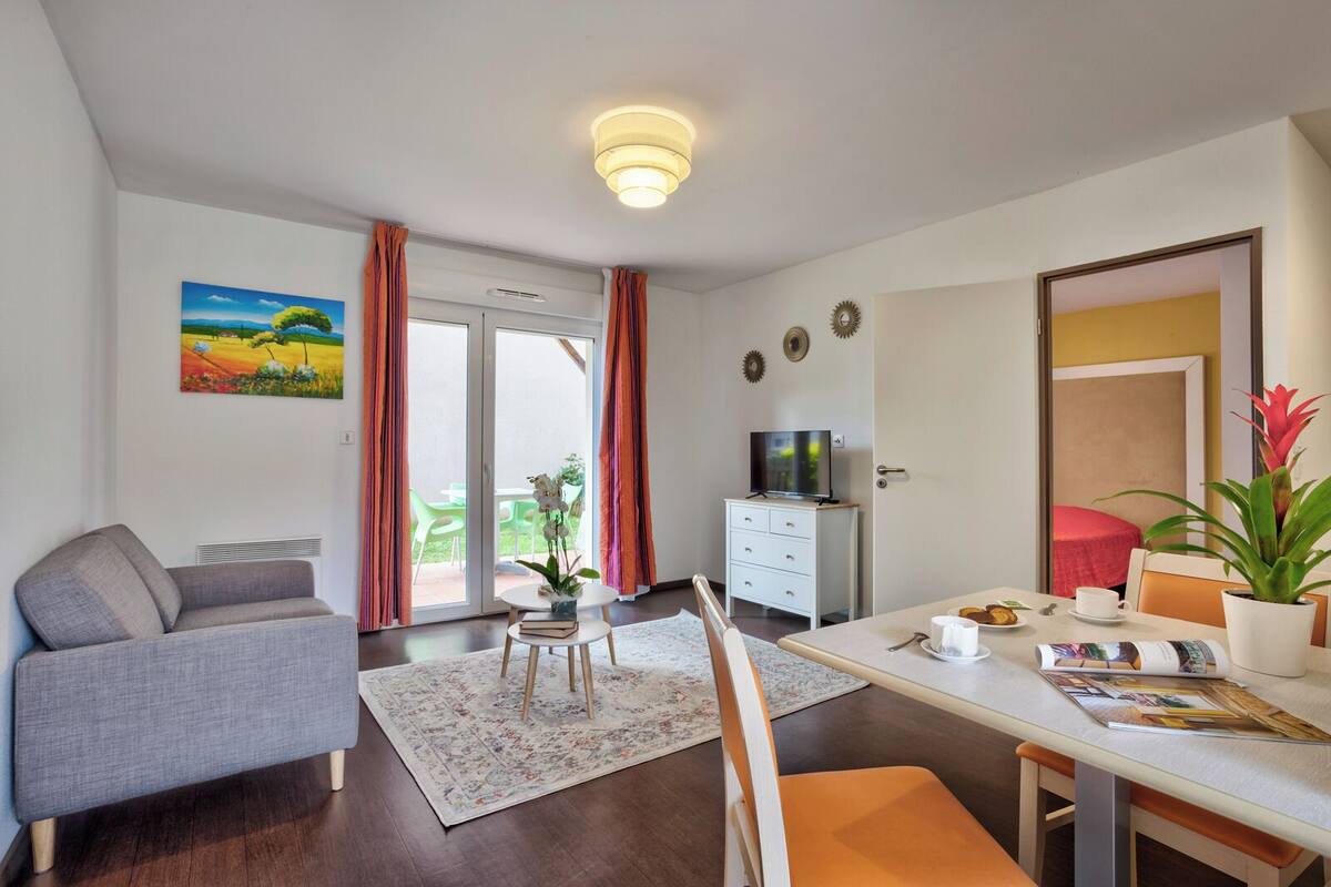 Een moderne woonkamer met een bank, een eettafel met stoelen, een televisie en een glazen schuifdeur naar een buitenruimte.