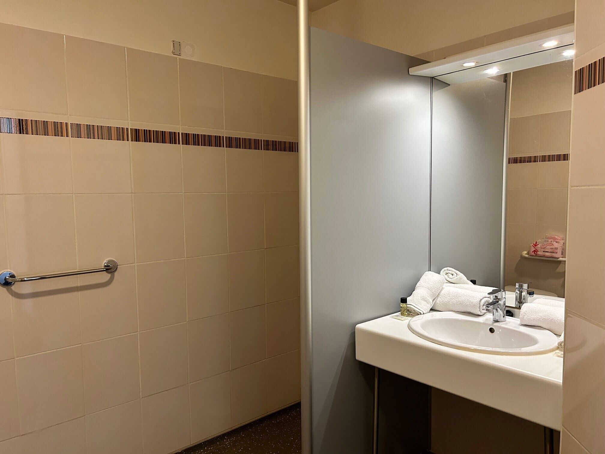 A bathroom with beige tiles, a towel rack, a sink with a mirror, and a shower area.