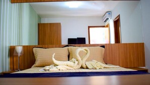Habitación de hotel con una cama, cabecero de madera, mesita de noche con lámpara y un equipo de aire acondicionado instalado en la pared.