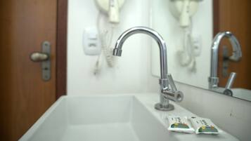 Une salle de bain avec un lavabo blanc, deux sèche-cheveux fixés au mur et une porte dotée d’une poignée.