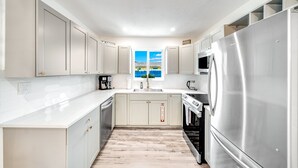 Een moderne keuken met witte kasten, roestvrijstalen apparatuur en uitzicht op het landschap door een raam.