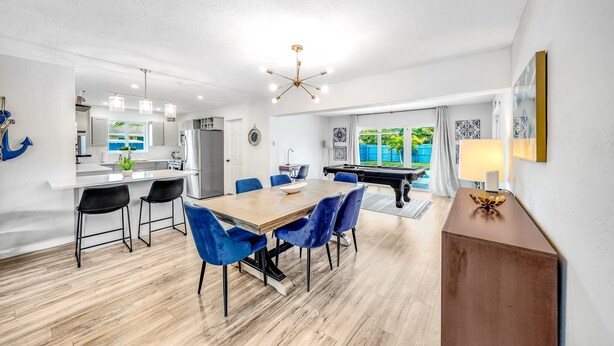 Een moderne keuken met witte kastjes, een eethoek met een houten tafel en blauwe stoelen, en een piano op de achtergrond.