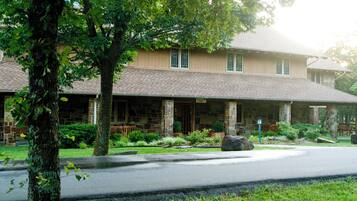 Traditional stone building with a pitched roof, set amidst a well-mainters front yard with mature trees and landscaped shrubbery.