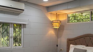A bedroom with a bed, a window, an air conditioning unit, and a wall-mounted light fixture.