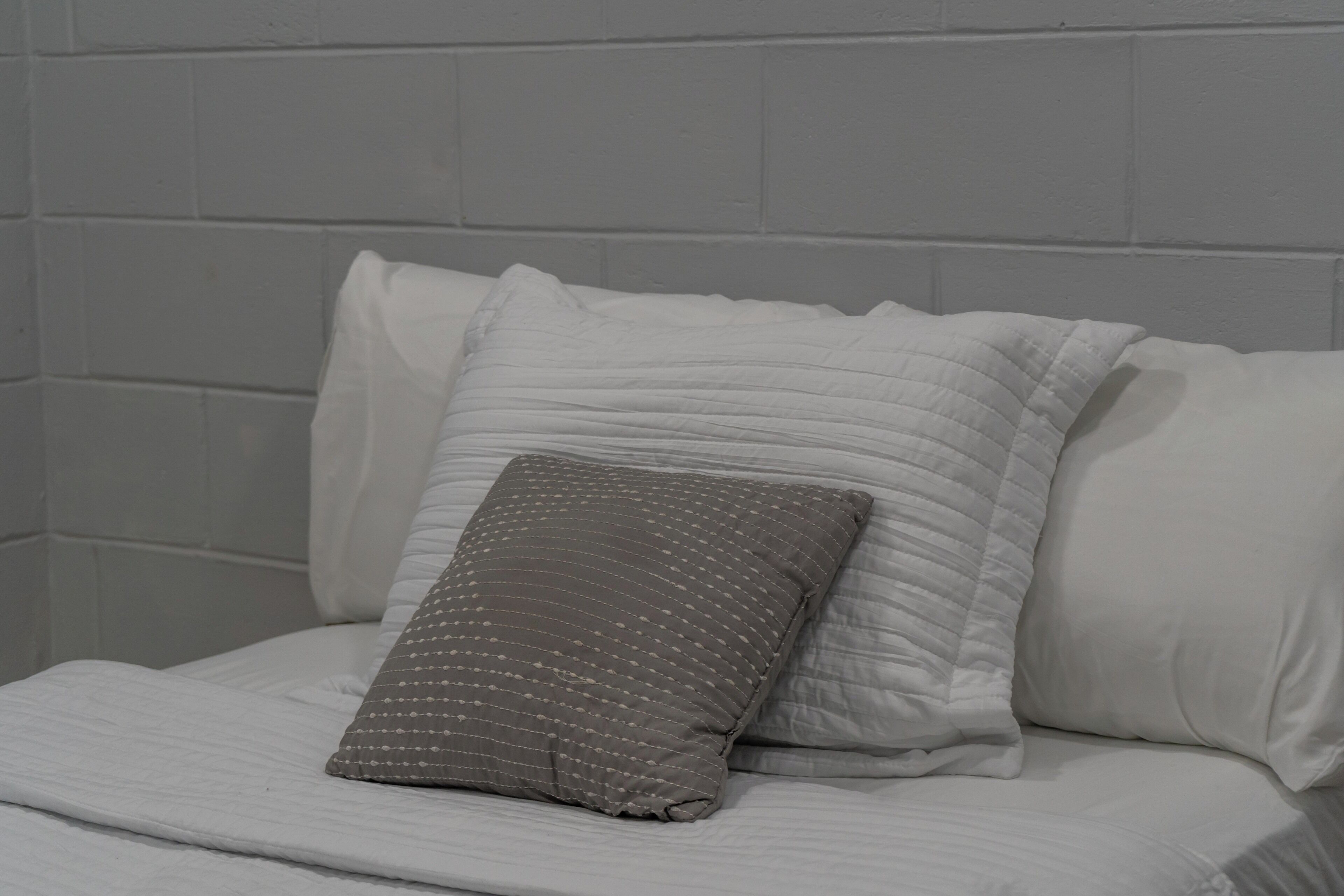 A bed with white bedding and a single gray pillow with a dotted pattern.