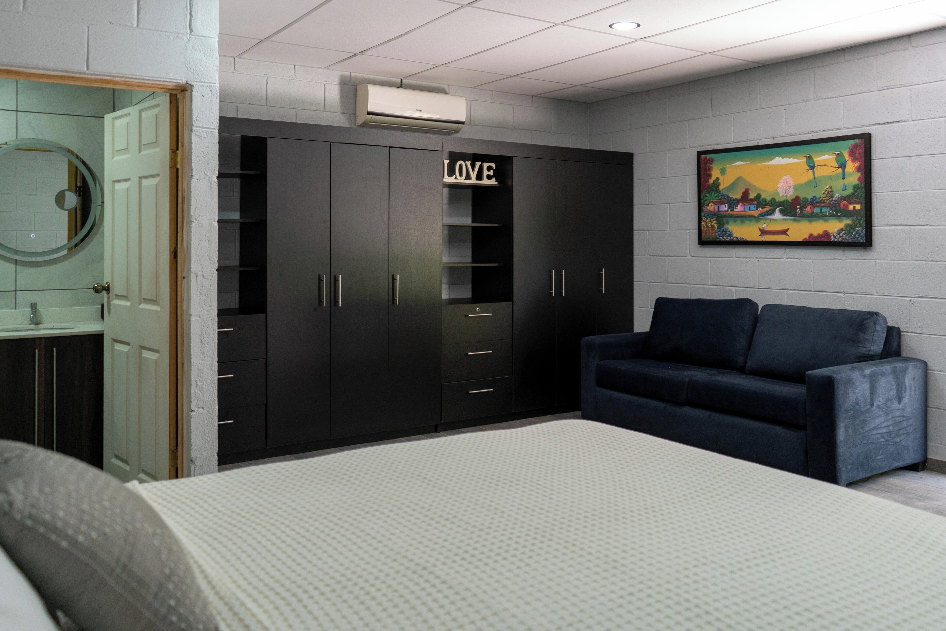 Une chambre à coucher avec un lit, une armoire de couleur sombre, un canapé bleu et un climatiseur fixé au mur.