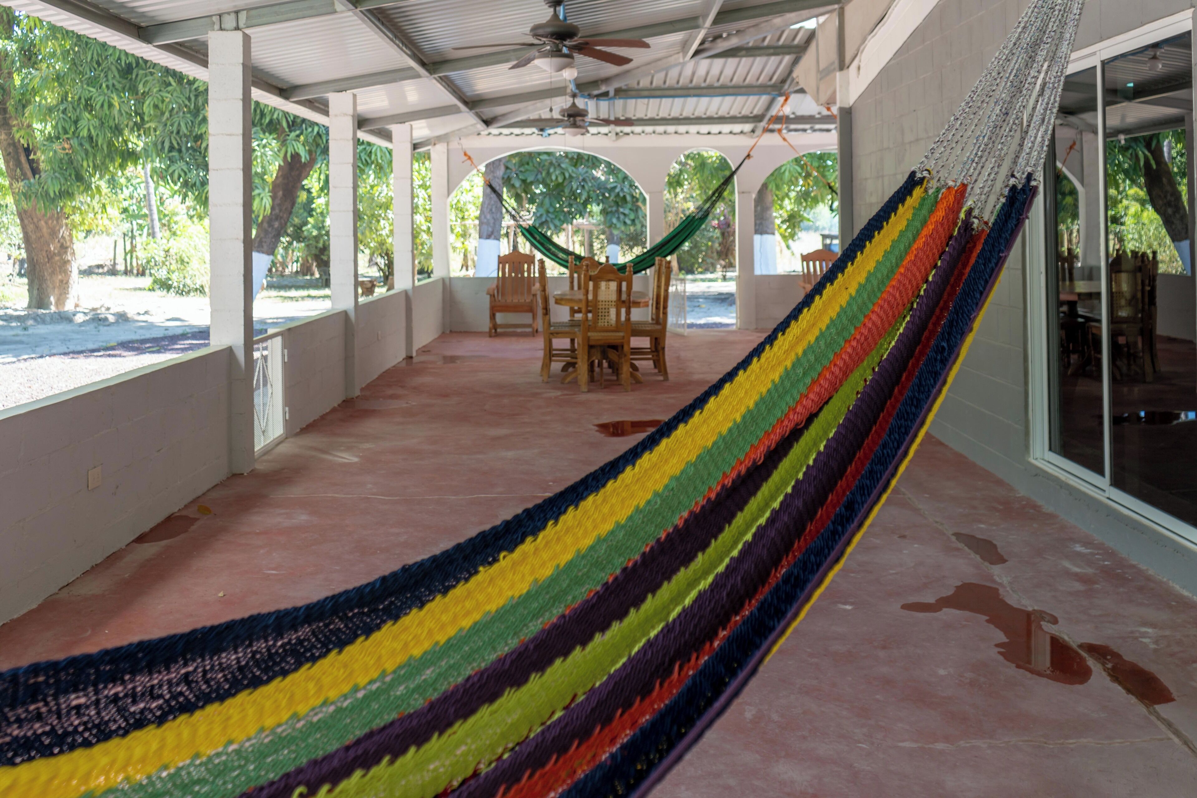 A covered outdoor area with a hammock, chairs, and a table.