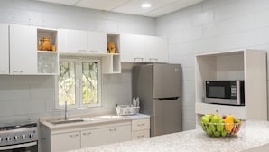 A modern kitchen with white cabinets, a stainless steel refrigerator, a microwave, and a fruit bowl on the counter.