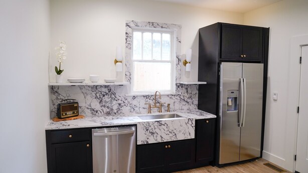 A modern kitchen with a marble countertop, black cabinets, a stainless steel refrigerator, and a built-in dishwasher.