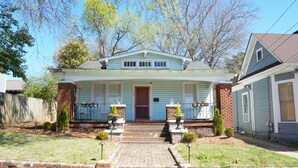A two-story house with a front porch, a red door, and a brick chimney.