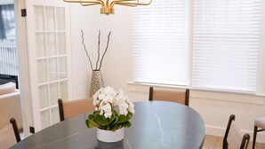 A dining area with a round table, chairs, a chandelier, and a vase with flowers.