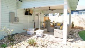 A covered patio area with outdoor furniture, a grill, and a small garden.
