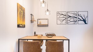A dining area with a wooden table, two chairs, a light fixture, and wall art. - Studio Augusta: modern, fully equipped, Rhine 50m, business & private, all-inclusive (Koblenz)