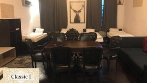 Habitación de hotel con una gran mesa de comedor de madera, cuatro sillas, dos camas individuales, un sofá de color oscuro y un ciervo montado en la pared.