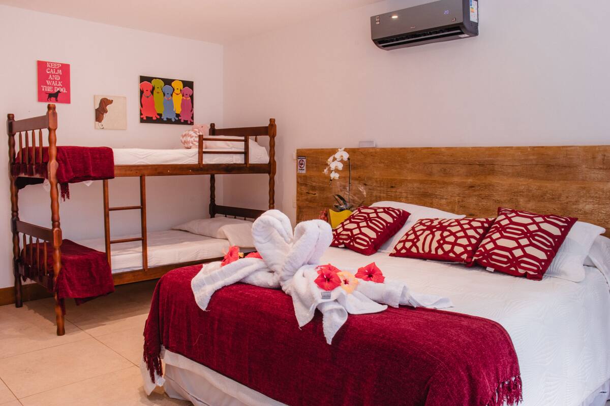 A hotel room with a bunk bed, a single bed with red bedding, and a wooden headboard.