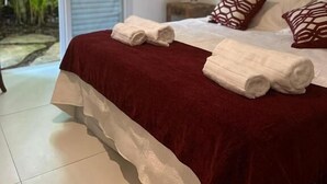 Un dormitorio con una cama grande, dos toallas enrolladas, un cabecero de madera y vista a la vegetación a través de una puerta corrediza.