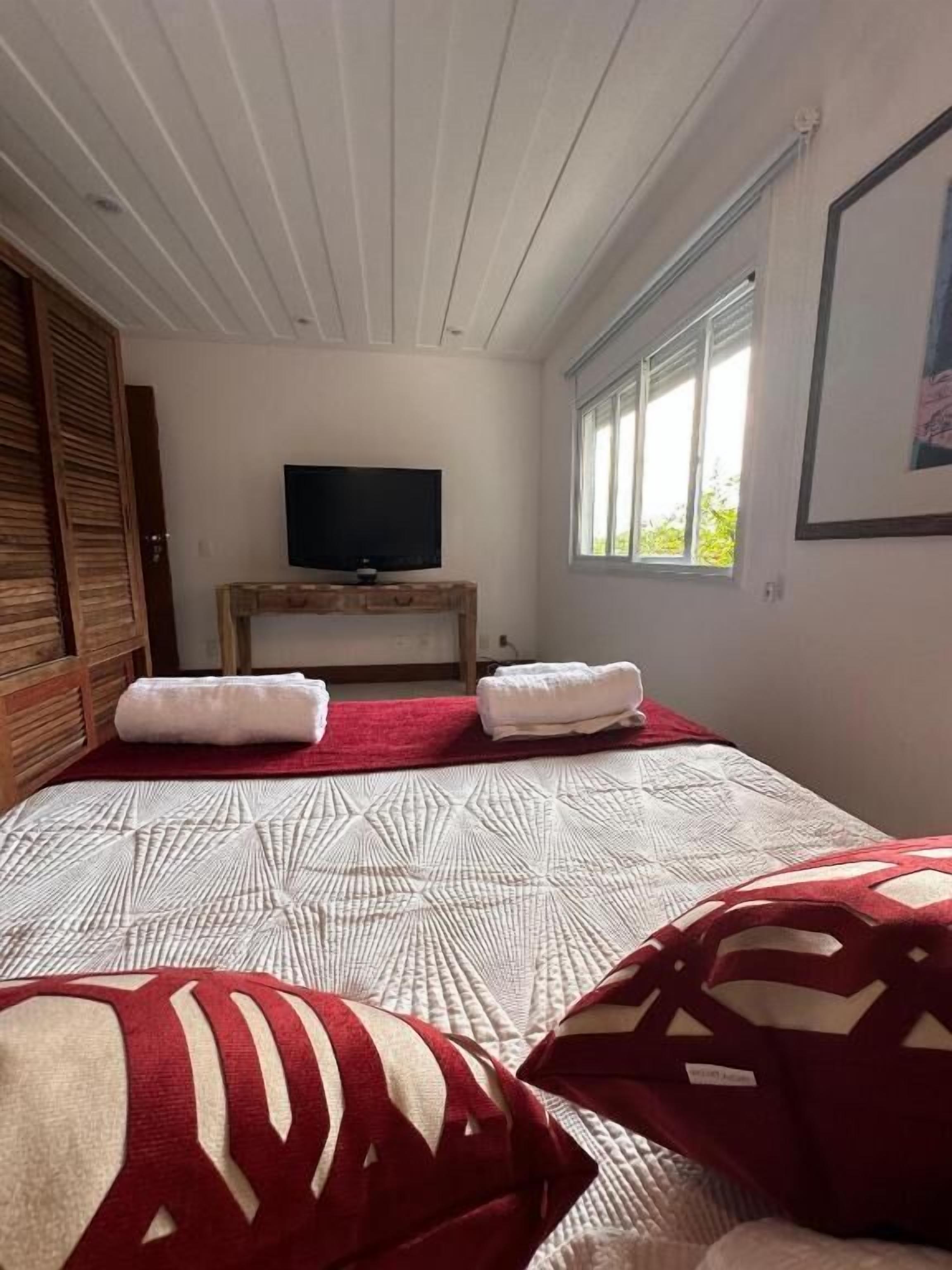Un dormitorio con cama, televisión sobre un mueble de madera, ventana y puerta.