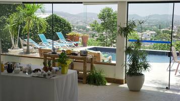 Terraço com piscina, espreguiçadeiras e uma mesa com comida e bebidas.