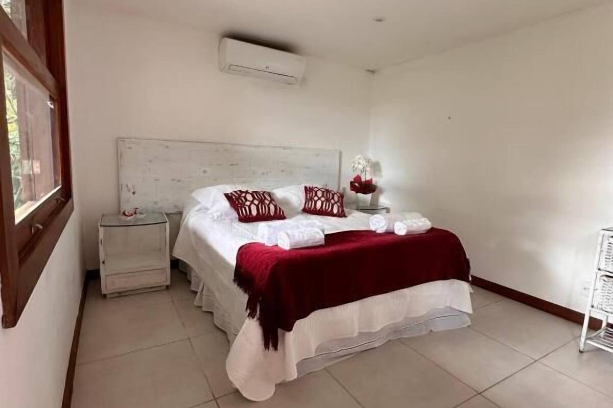 A bedroom with a bed, a nightstand, a bedside table, and an air conditioning unit.