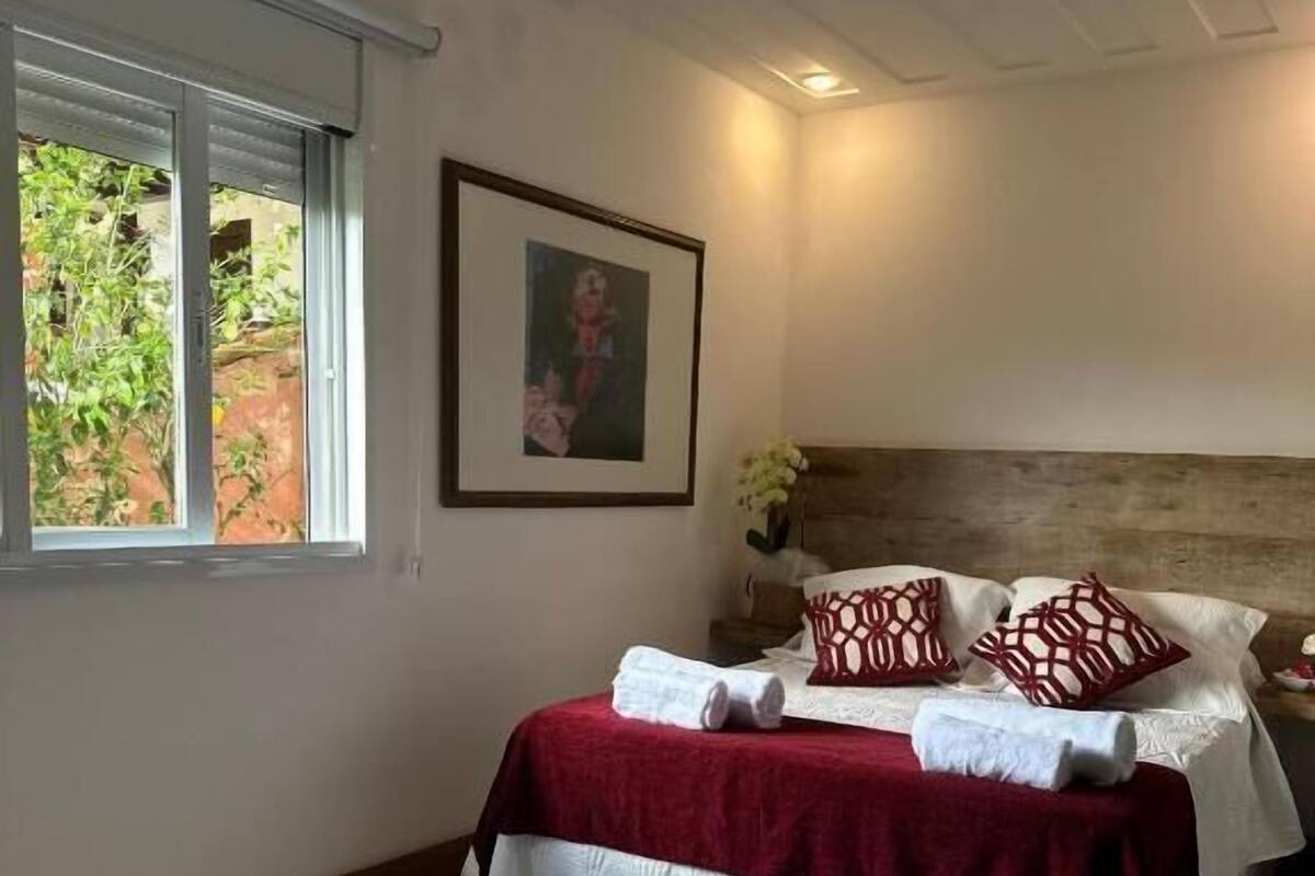 A bedroom with a bed, a window, and a framed picture on the wall.
