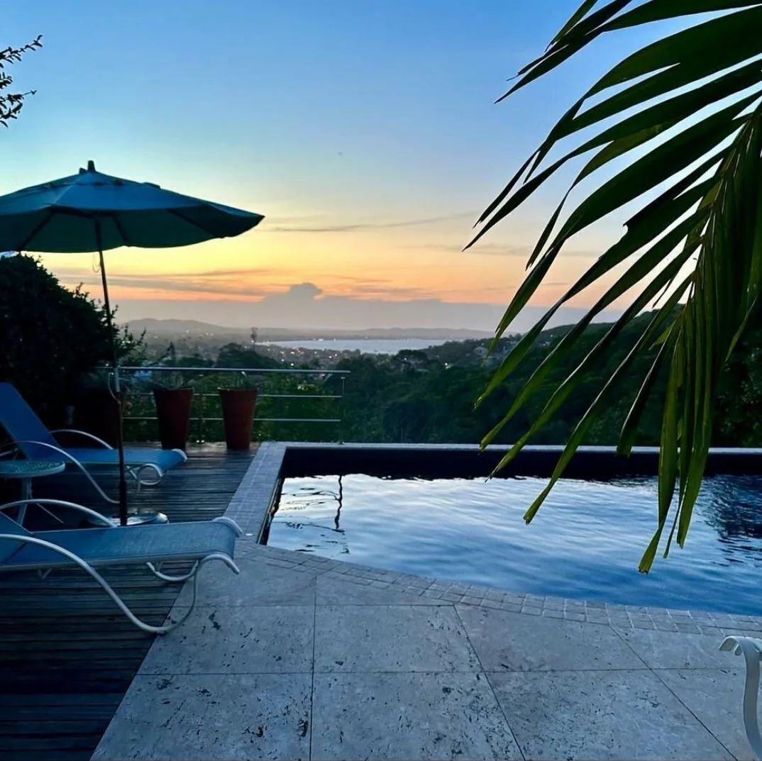 Piscina no terraço com vista para a cidade ao pôr do sol.