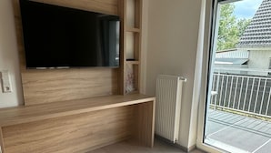 Una sala de estar moderna con un televisor de pantalla plana grande montado en una pared de madera, un banco empotrado y un amplio ventanal corredizo que da a un balcón.