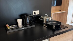 Una cocina moderna con encimera negra, cafetera, hervidor, sartén y olla. Hay un cajón blanco con el nombre de la marca 