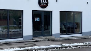 Un hotel B&S con una fachada moderna, ventanas amplias y un detalle rojo en la parte superior del edificio.
