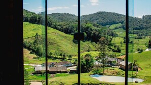 A room with a large window offering a view of a green landscape with hills and a small body of water.