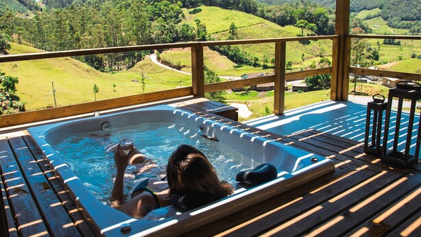 A hot tub on a wooden deck with a view of a green landscape.