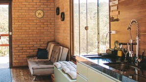 A cozy cabin interior with a wooden ceiling, brick walls, a sofa, and a kitchen area with a sink and utensils.