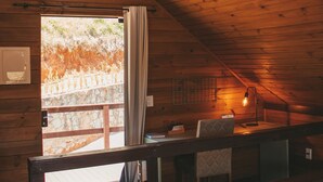 A wooden interior with a sloped ceiling, a bench seating area, and a view through a doorway.