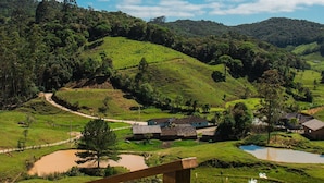 A scenic view of a lush green valley with a winding path, a small pond, and a few houses.