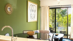 A room with a green wall, a framed artwork, a dining area with a table and chairs, a window with curtains, and a view of greenery outside. - Cap Cana Luxury 2 bedroom and 2 bath condo, Pool, near Juanillo beach, Golf




 (Las Canas)