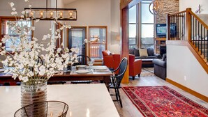 A spacious living room with a dining area, a staircase, and large windows offering a view of the outdoors. - 385 Moonshine Crescent by Okanagan Premier (Beaverdell)