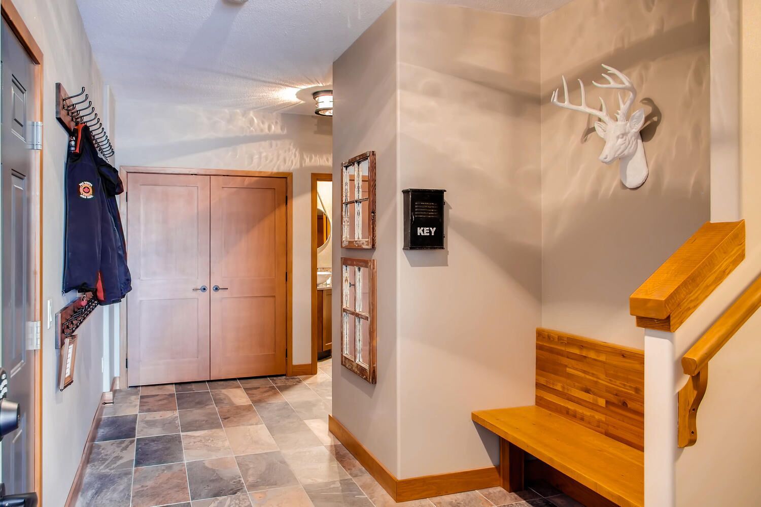 A hallway with a wooden bench, a coat rack with sports gear, a door, and a wall-mounted keybox.