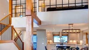 A spacious loft-style apartment with a wooden staircase, a kitchen with a large island, and a dining area with a chandelier. - 385 Moonshine Crescent by Okanagan Premier (Beaverdell)