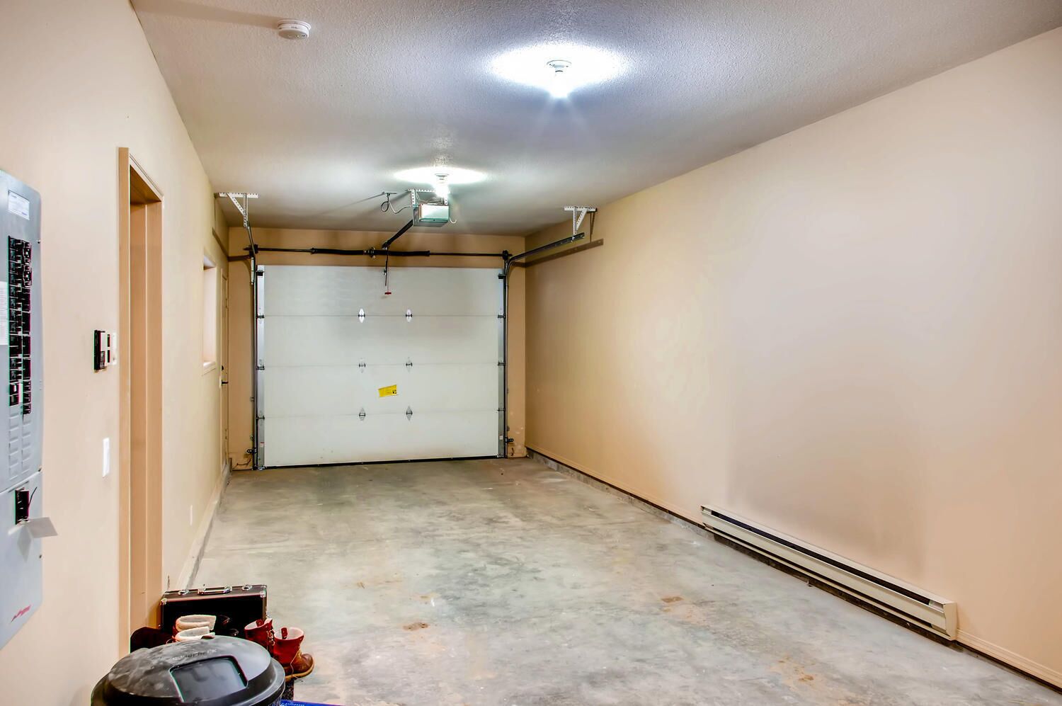 En ren og tom garage med lukket garageport, et loftslys og en vægmonteret termostat.