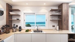 Uma cozinha moderna com vista para o oceano, com uma pia dupla, prateleiras de madeira e bancada com diversos utensílios de cozinha.