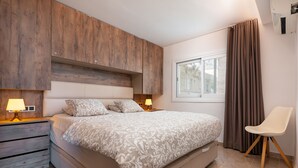Quarto moderno com cama grande, cabeceira de madeira, abajures e janela com cortinas.