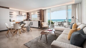 Sala de estar moderna com sofá, mesa de centro e área de jantar. Há uma janela grande com vista para o oceano.