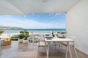 Ein Balkon mit Essplatz, der auf einen Strand mit Menschen und Sonnenschirmen blickt.