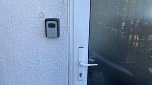 Eine weiße Tür mit Fensterglas, Klingel und einer Wandleuchte.