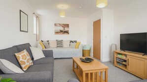 Ein modernes Wohnzimmer mit einem grauen Sofa, einem Holztisch und einem Fernseher auf einem Holzboden.