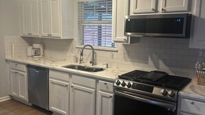 A kitchen with white cabinets, a stainless steel stove, a microwave, and a window with blinds. - Vacation Paradise in Jonesboro (Jonesboro)