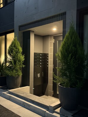 A modern building entrance with a glass door, potted plants, and a metal gate. - Tasuki Smart Kinshicho II (Tokyo)