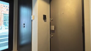 A hallway with a dark door, a lighter door, and a window with a view of a brick building. - Tasuki Smart Kinshicho II (Tokyo)