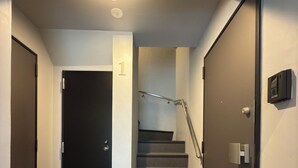 A modern staircase with a handrail, a door with a number sign, and a wall-mounted intercom. - Tasuki Smart Kinshicho II (Tokyo)