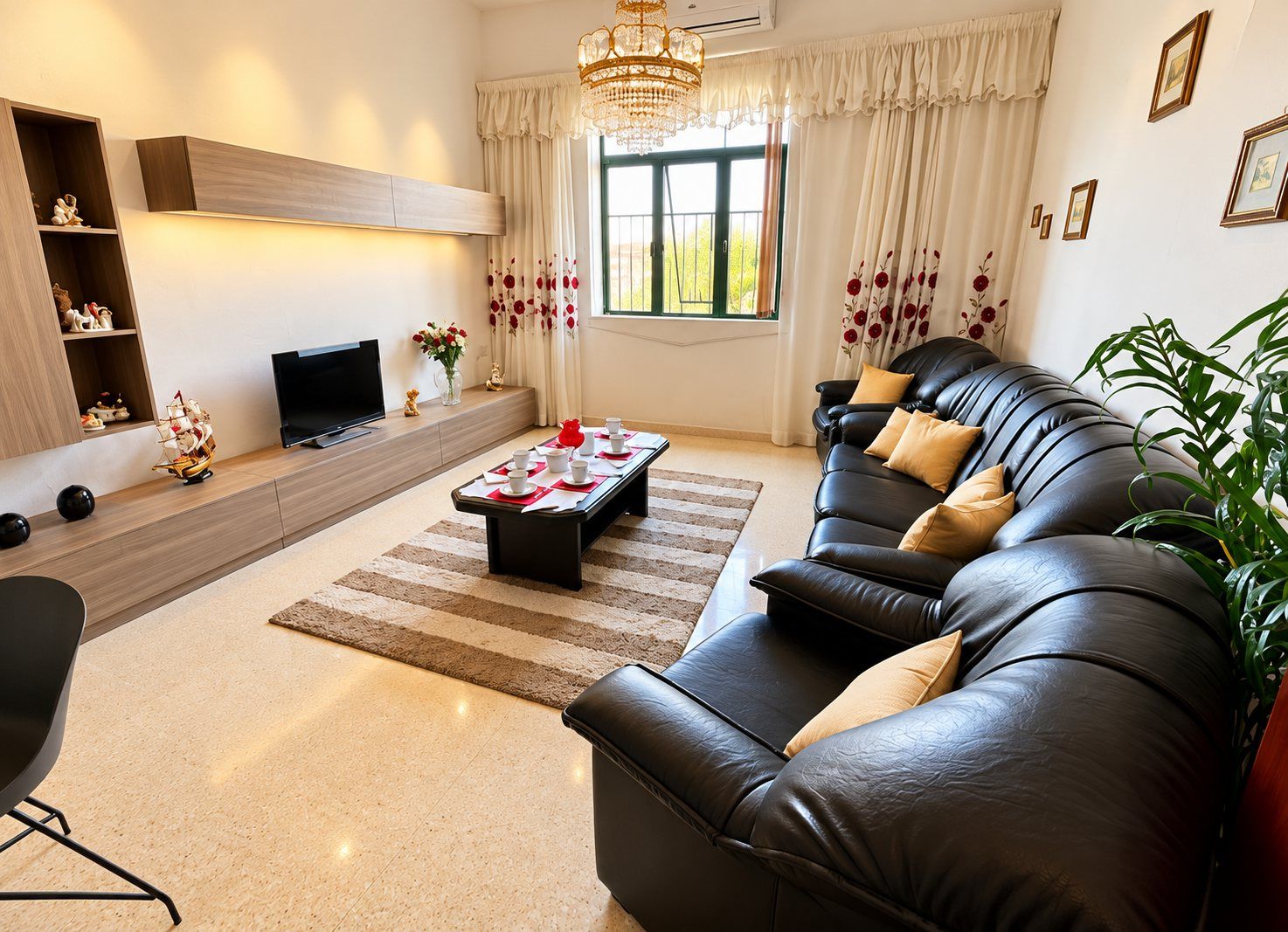 A modern living room with a leather sofa, a flat-screen TV, a coffee table, and a large window with curtains.
